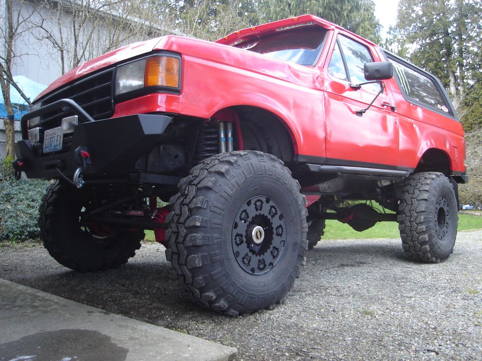 Red lifted Ford Bronco with big tires and custom bumper. License plate reads 'CORFLEX'