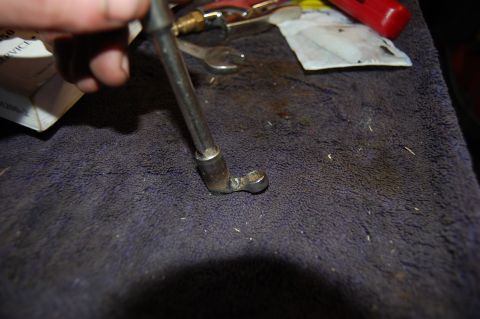 1994 Ford Bronco - A hand holds a metal tool with a socket end over a dark cloth, with other tools and a red object in the background.