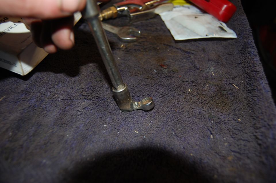 Close-up of a metal tool with a socket end, held by a hand, on a dark cloth surface