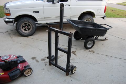 1994 Ford Bronco - A shop-built black steel engine or transmission dolly with small casters stands on a driveway, with a white OBS Ford Bronco parked behind i…
