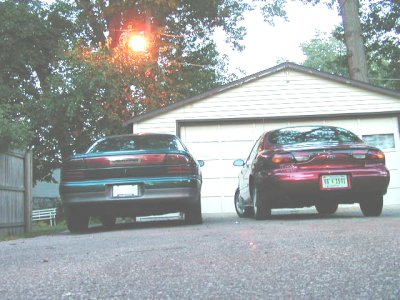 1997 Ford Taurus - Two sedans, including a 1997 Ford Taurus, are parked in front of a garage.