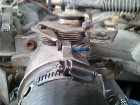 1989 Ford Bronco - Close-up view of a vehicle's throttle body assembly, showing mechanical components and a hose clamp.