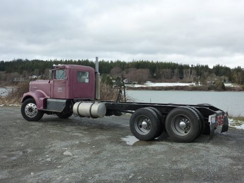 1959 Kenworth W900A - A bare chassis semi-truck sits idle near a lake under an overcast sky.