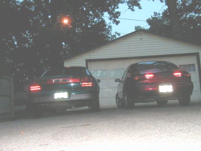 1997 Ford Taurus - Two sedans are parked in front of a garage. The image has a watermark at the bottom right.