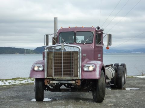 1959 Kenworth W900A - A purple semi-truck cab is parked near the water on an overcast day.
