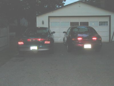 1997 Ford Taurus - Two sedans are parked in front of a garage door at dusk. One vehicle has a visible license plate.