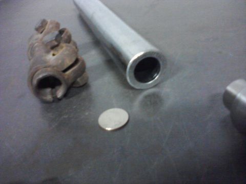 1971 International School Bus - Close-up of automotive parts, including a U-joint and a metal tube, on a textured surface.