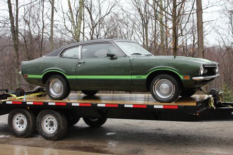 1985 Ford Bronco - A green Ford Maverick coupe is transported on a flatbed trailer.