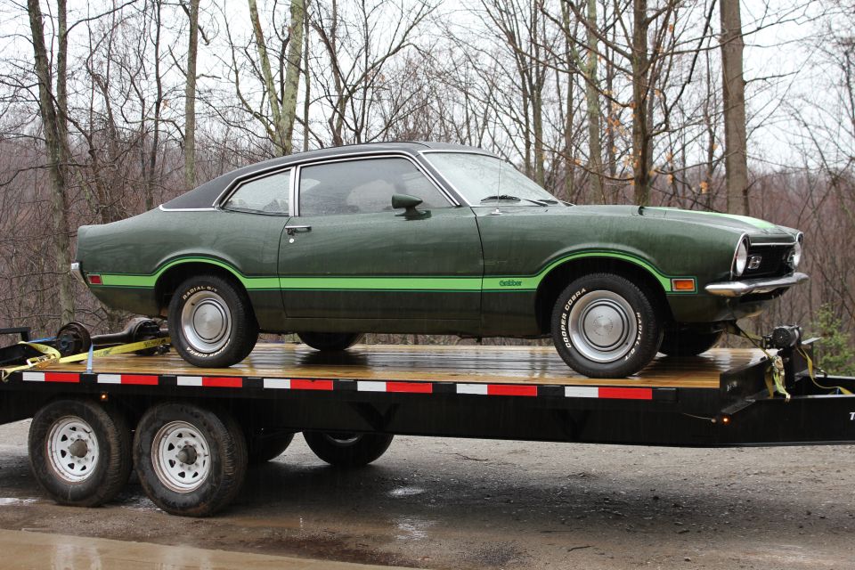 Green Ford Maverick coupe on a flatbed trailer, side view with green racing stripes