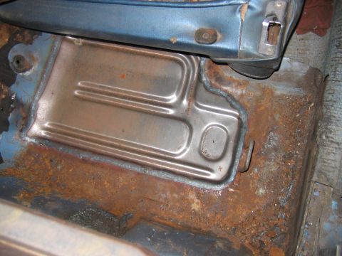 1971 Ford Ranchero - The floor pan of a vehicle shows significant rust and a metal cover plate, with a portion of the blue seat visible.