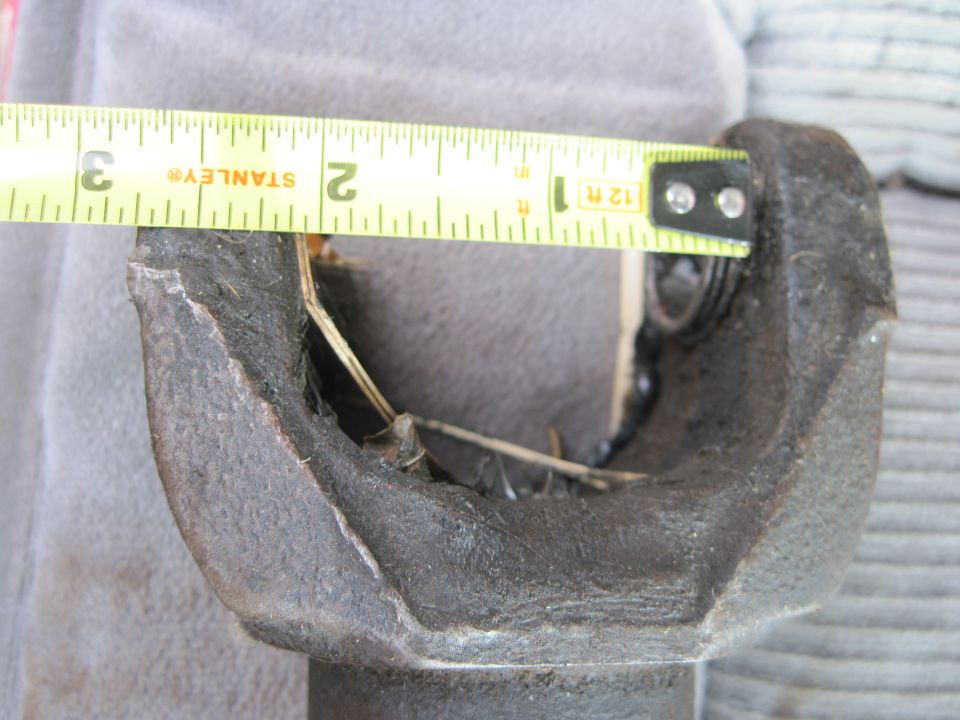 Measuring a damaged driveshaft U-joint with a tape measure. The joint appears to be failing