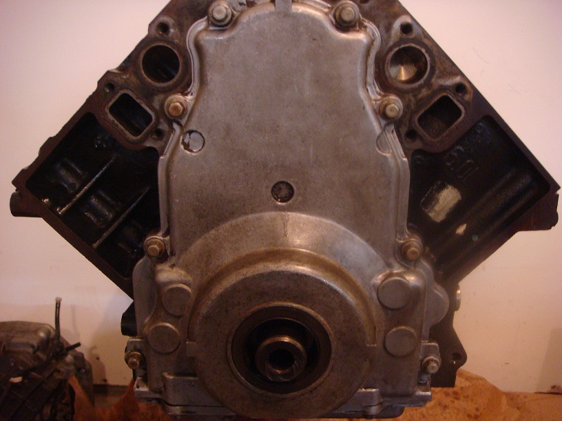 Engine block with a silver timing cover and black cylinder heads. A circular metal component is visible at the bottom center