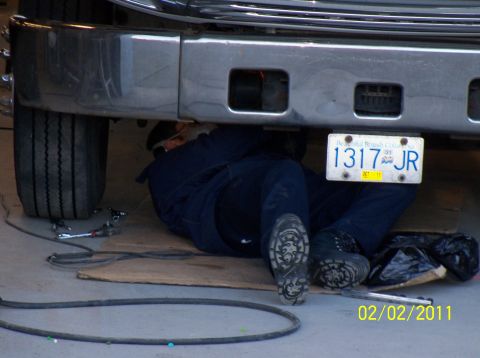 1989 Ford Bronco - A mechanic is working underneath a vehicle, with a license plate clearly visible.