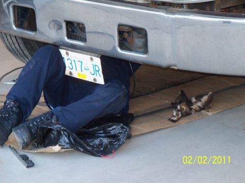 1989 Ford Bronco - A person is working underneath a vehicle, with a license plate visible on the front bumper.