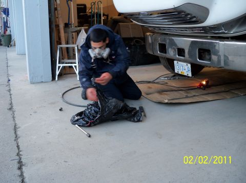 1989 Ford Bronco - A person wearing a respirator works on the underside of a vehicle, near the rear bumper and tire. The date 02/02/2011 is visible.