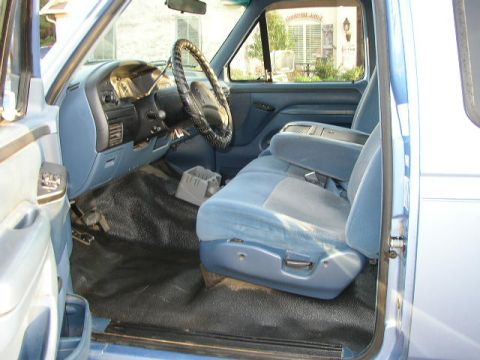 1995 Ford Bronco - The interior of a blue truck shows the dashboard, steering wheel, and light blue seats with a center console.