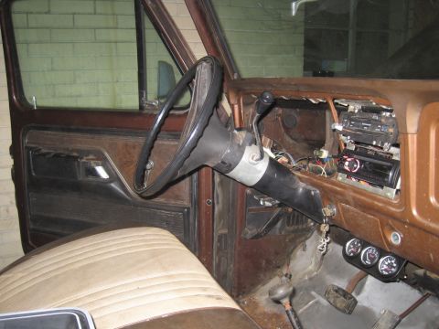 1979 Ford Bronco - The interior of an older vehicle shows a worn dashboard with aftermarket gauges and a radio installed.
