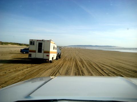 1996 Ford Bronco - Truck and camper driving on a beach with tire tracks in the sand.