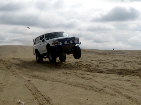 1996 Ford Bronco - 1996 Ford Bronco catches air while driving on a sand dune under a cloudy sky.