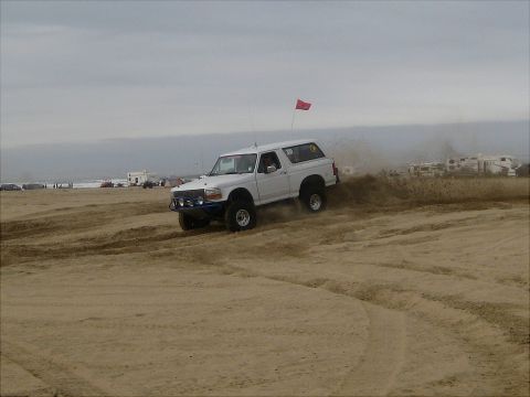 1996 Ford Bronco - A white Ford Bronco navigates a sandy terrain, kicking up dust as it goes.