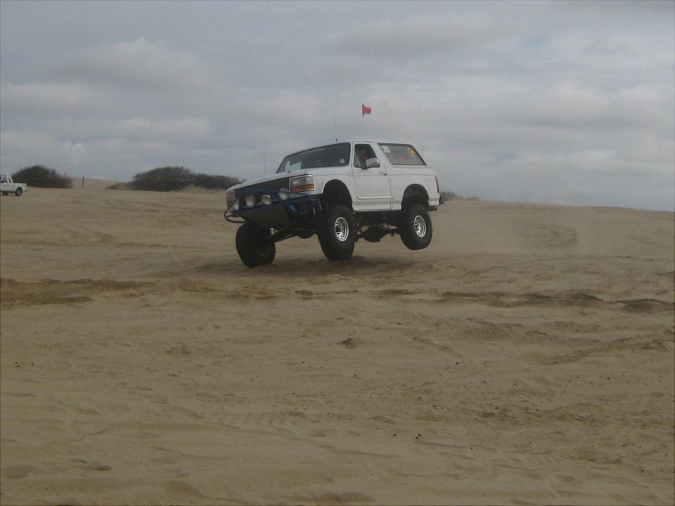 White 1996 Ford Bronco airborne over sand dunes