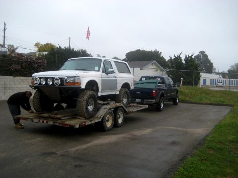 1996 Ford Bronco - A person loads a modified 1996 Ford Bronco onto a trailer towed by a pickup truck.