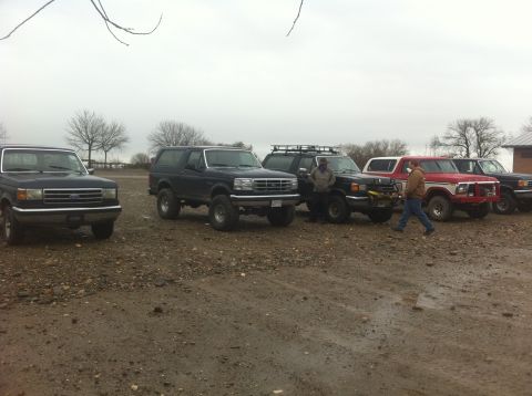 1990 Ford Bronco - Several Ford Broncos and trucks are gathered in a gravel lot on an overcast day.