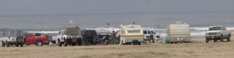 1984 Ford Bronco - A collection of trucks, SUVs, and campers are parked on the sand near the ocean waves.