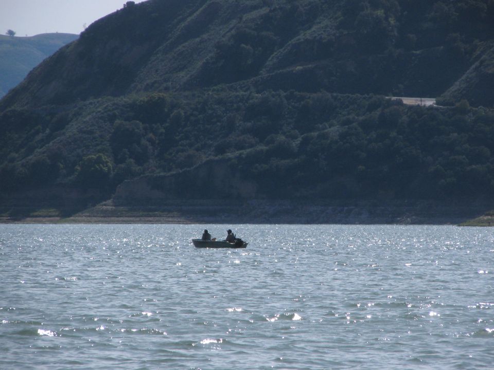 Two people in a small boat on a lake, with a tree-covered hill in the background