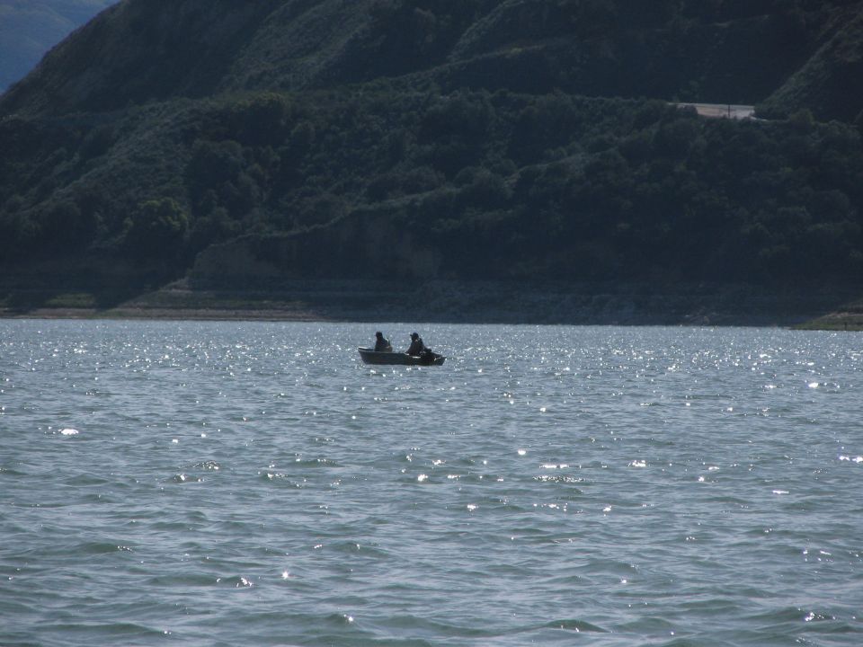 Small boat with two people on a sparkling blue lake, with a tree-covered hill in the background