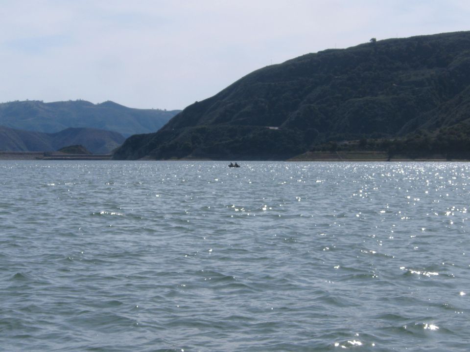 Two people in a small boat on a sparkling lake with tree-covered hills in the background