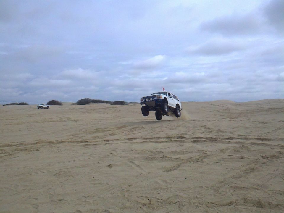 1994 Ford Bronco airborne over sand dunes with another vehicle in the distance