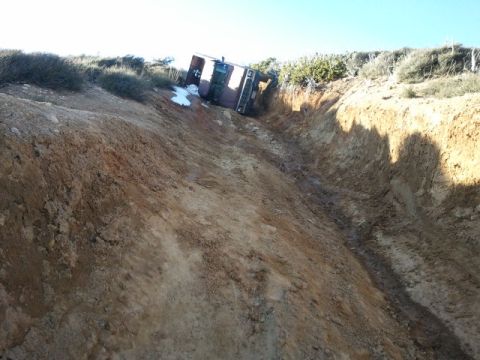 1978 Ford Bronco - A vehicle is precariously positioned in a deep, narrow ditch on a sunny day.