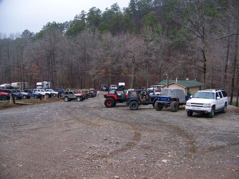 1992 Jeep YJ - A 1992 Jeep YJ is parked in a lot filled with other vehicles, surrounded by trees and a small building.