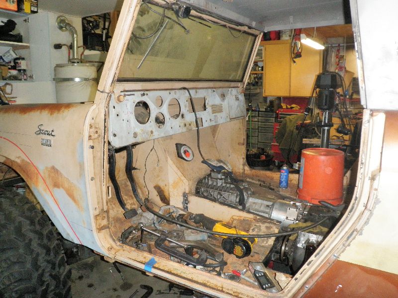 1961 International Scout 800 interior, showing disassembled dashboard, transmission tunnel, and driver's side door panel. Vehicle is in a state of restoration