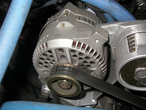 1990 Ford Bronco - Close-up of a large cast-aluminum alternator mounted in an engine bay, with copper windings visible through its vented case and a serpentin…