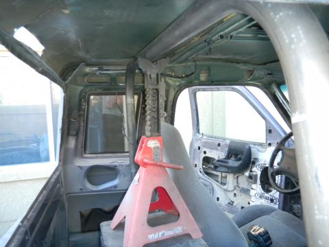 1997 Ford Ranger - The interior of a truck is shown with a roll cage installed and the door panels removed, with a jack stand supporting the frame.