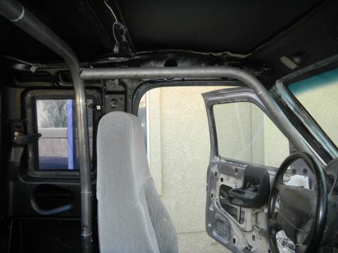 1997 Ford Ranger - The interior of a vehicle shows a custom roll cage installation and a gray seat, with the door removed.