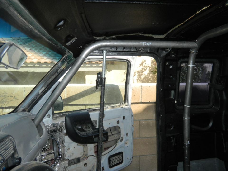 Roll cage tubing inside stripped pickup cab, bare white door and foil insulation