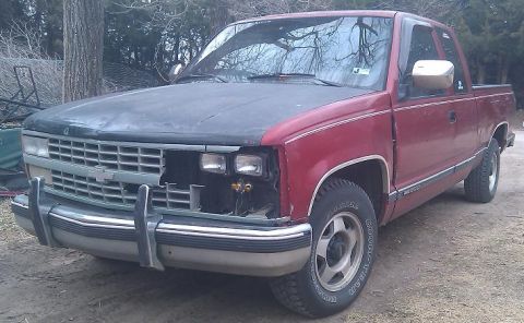 2000 Mercury Grand Marquis - A red pickup truck sits outside with its hood a different color and damage to the front end.
