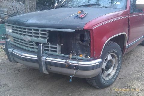 2000 Mercury Grand Marquis - A red pickup truck with its front end disassembled sits outdoors, showing exposed wiring and tools on the hood.