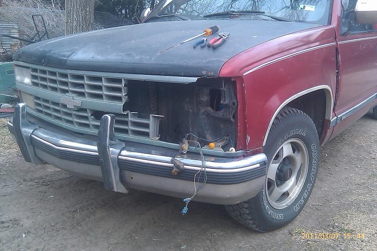 Red Chevrolet pickup with headlight removed showing exposed header panel and loose wiring