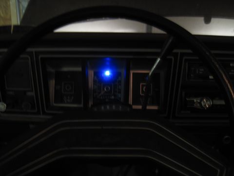 1979 Ford Bronco - The interior of a vehicle shows the dashboard with gauges and a steering wheel, illuminated by a blue light.