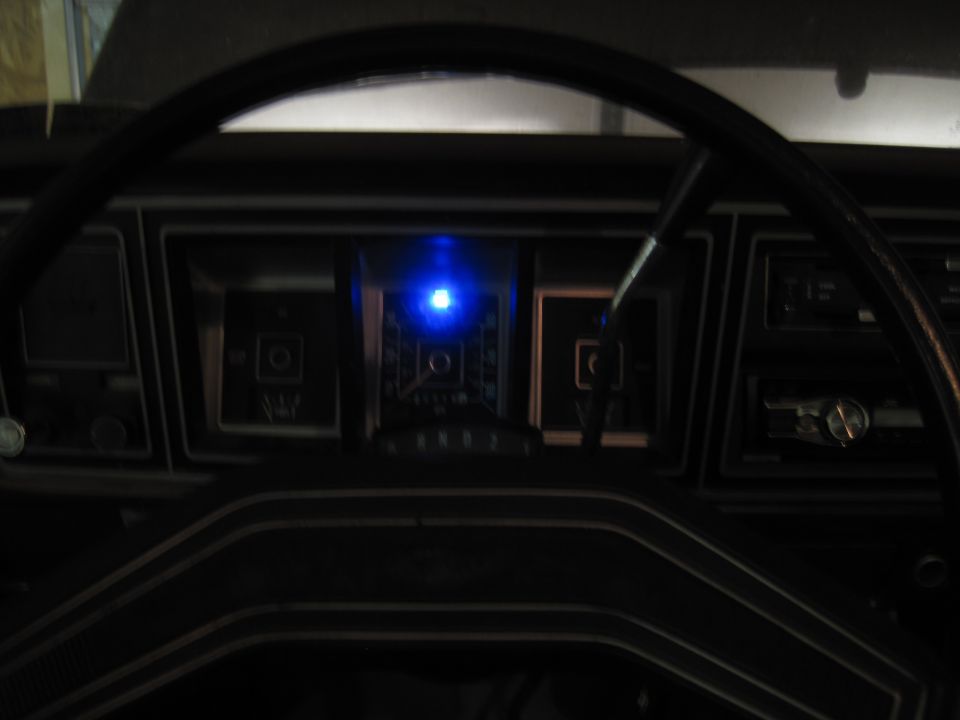 Dashboard with steering wheel and lit up gauges. Blue light is on