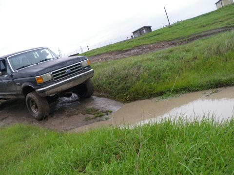 1991 Ford Bronco - A Ford truck navigates a muddy obstacle on a cloudy day.
