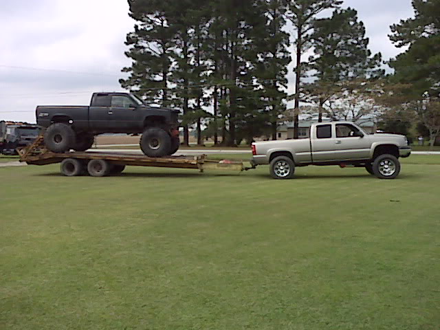 Black lifted pickup on trailer towed by silver lifted pickup