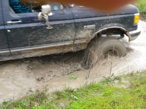 1991 Ford Bronco - This Ford F-250 is navigating a challenging muddy terrain, with water splashing around its tires.