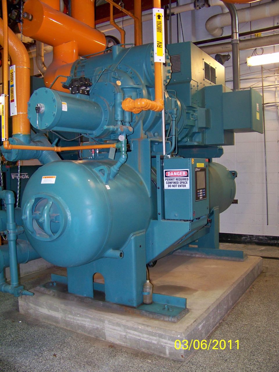 Turquoise industrial chiller unit with orange pipes and danger signs
