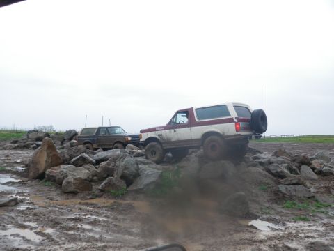 1991 Ford Bronco - Two Ford Broncos tackle a challenging off-road course filled with mud and rocks.