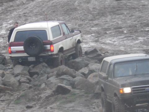 1991 Ford Bronco - Two Ford Broncos tackle a challenging off-road course filled with rocks and mud.